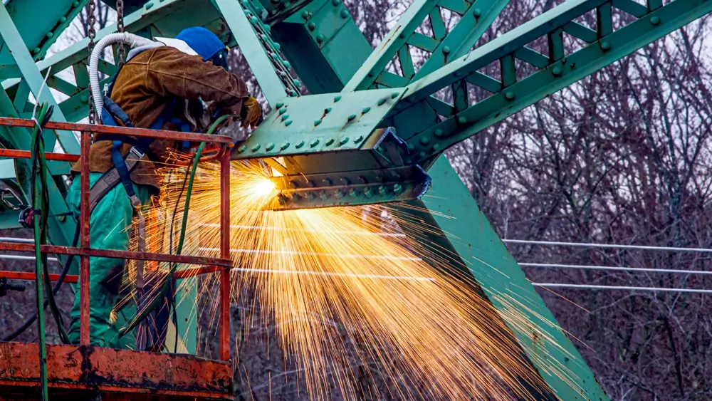 A person cutting the metal on a bridge to dismantle it